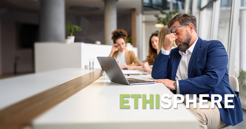 Stressed businessman rubbing his eyes while working over laptop with females colleagues in the background