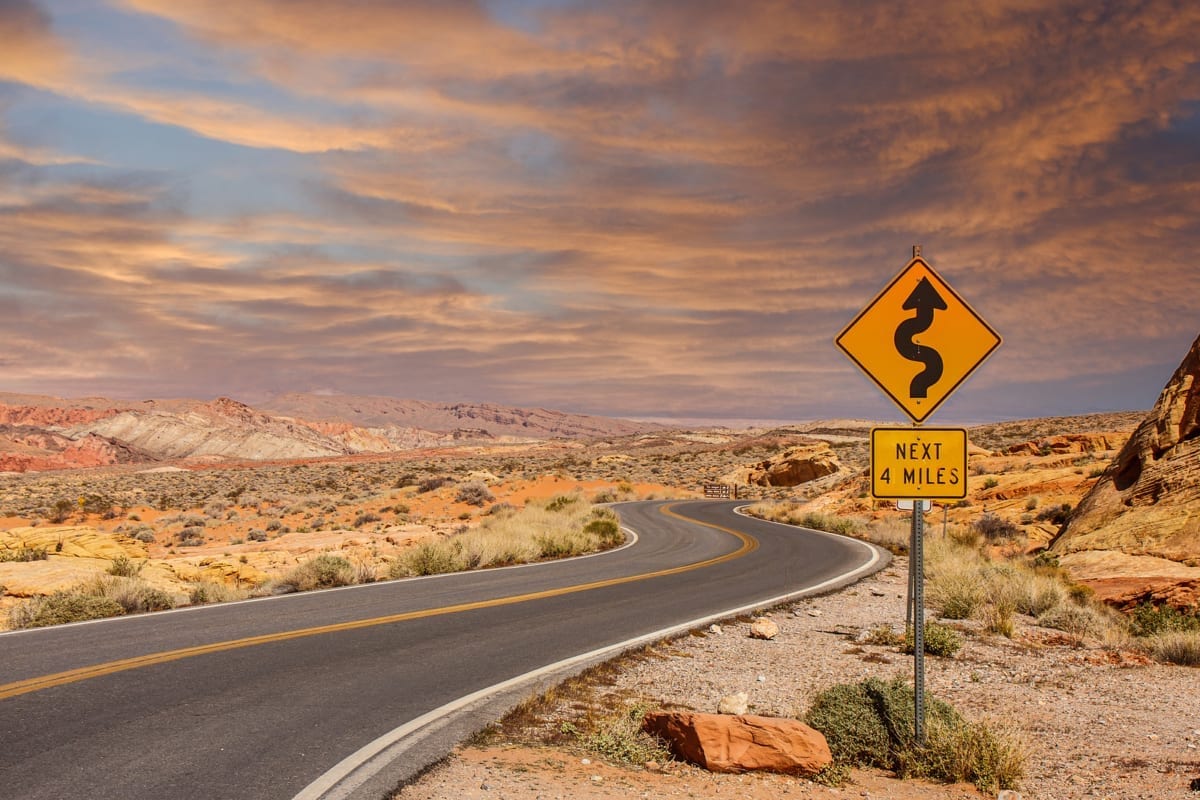 A Road Sign In The Middle Of A Desert Showing Curves Ahead desert road